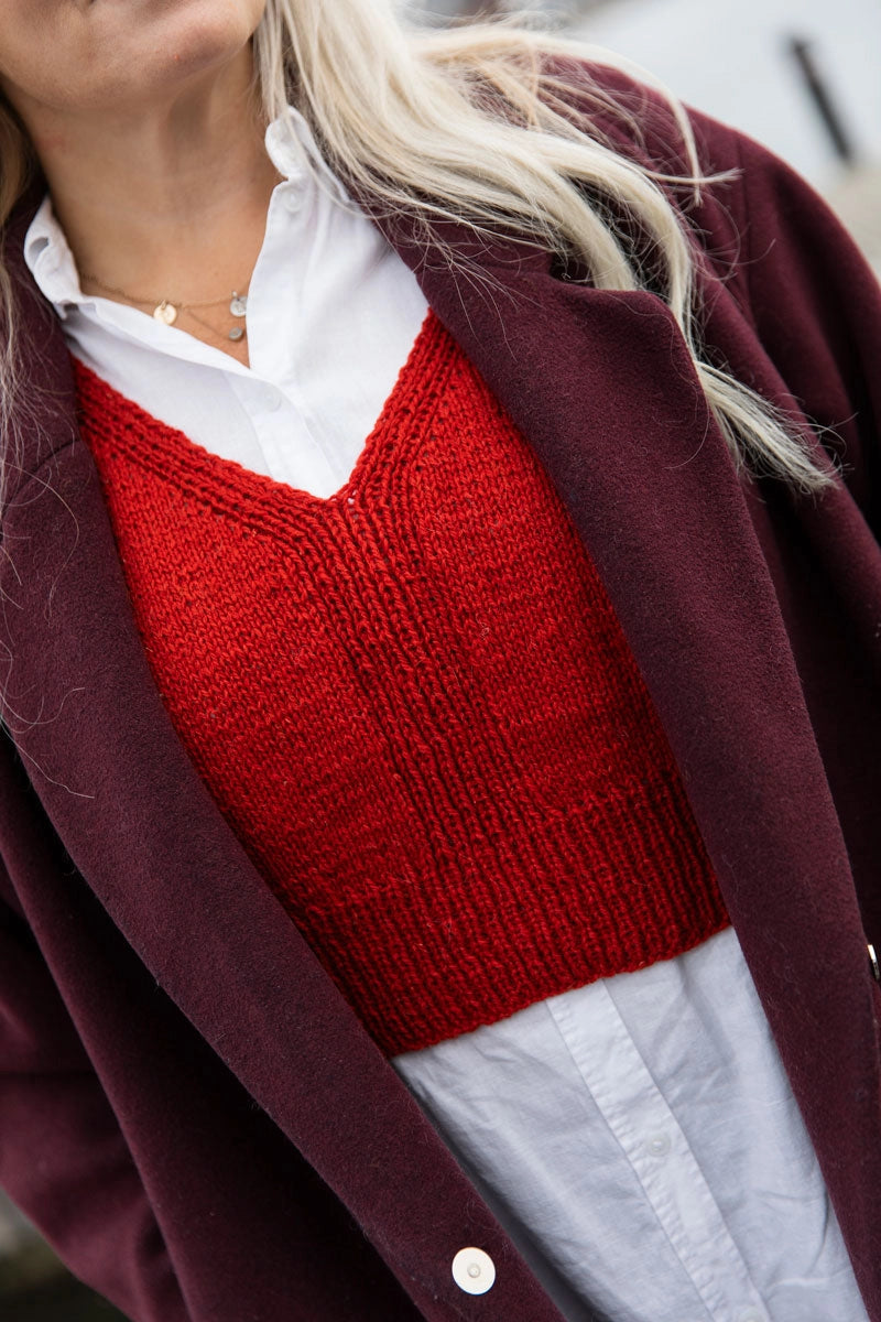 a cropped red knit vest worn over a white blouse