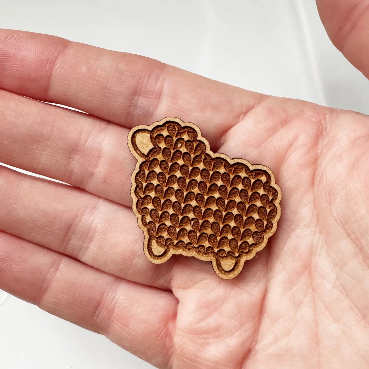 Wooden sheep-shaped needle minder held in a hand against a white background