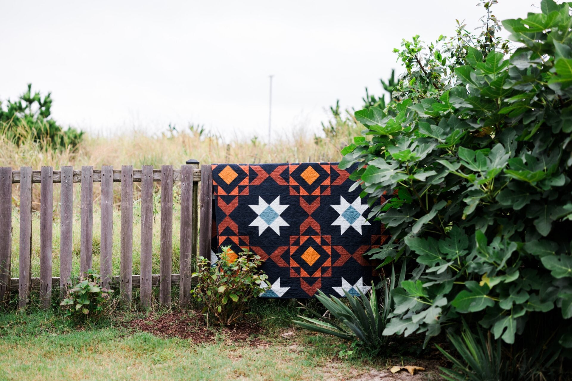 Quilt with geometric pattern draped over a wooden fence in a garden setting