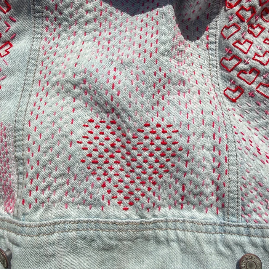 Close-up of a denim jacket with red stitching on grass