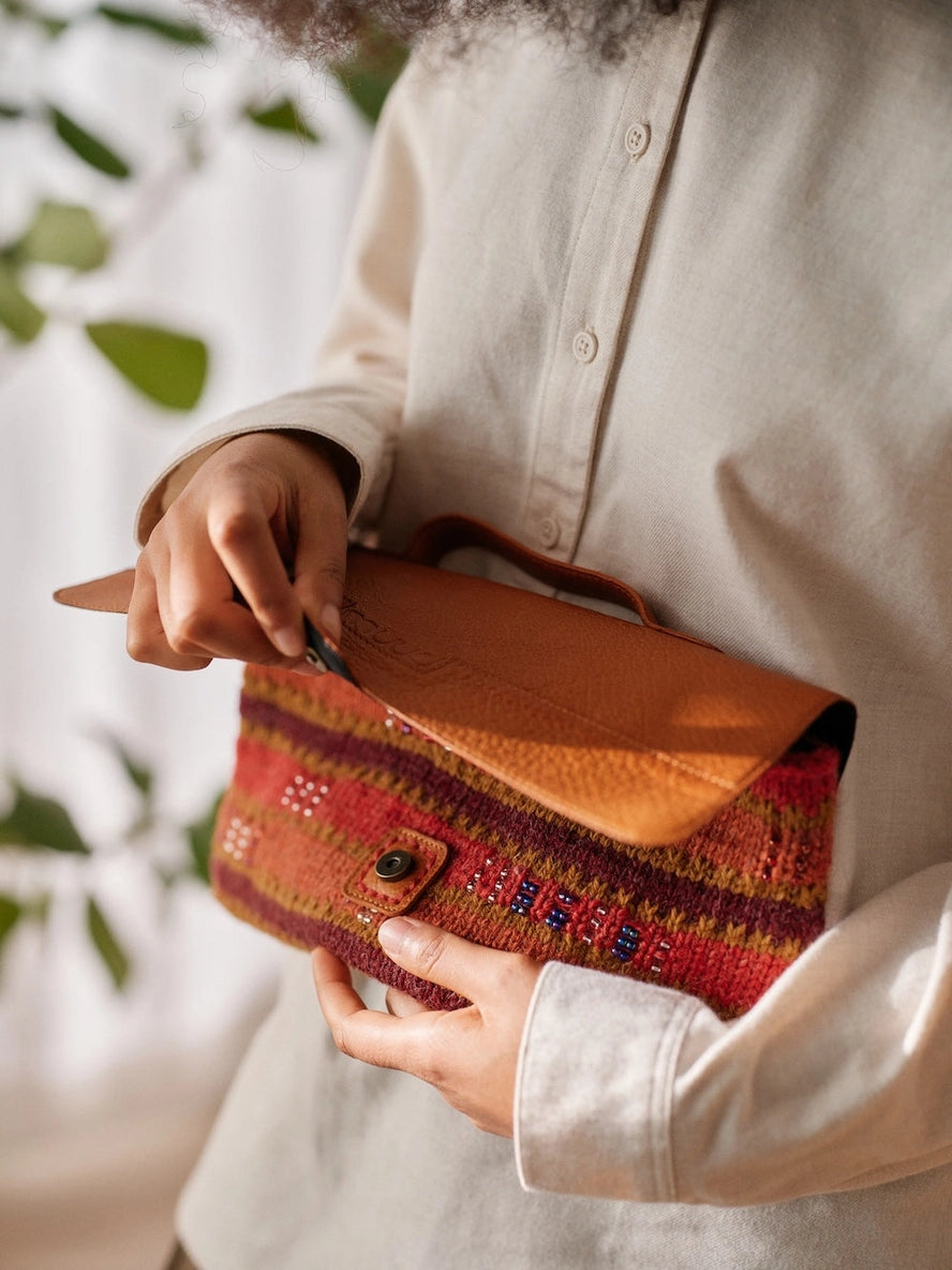 Person holding a brown leather clutch with a colorful pattern