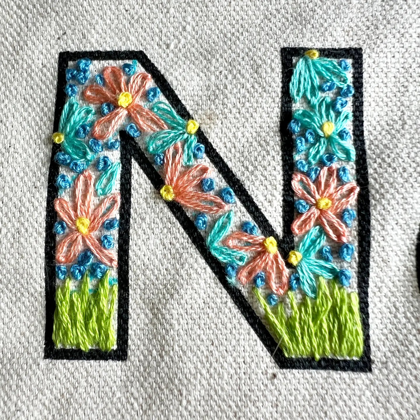 Embroidered letter 'N' with floral designs on a fabric background