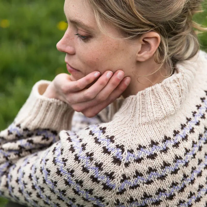 Woman wearing a patterned sweater sitting outdoors with green grass in the background