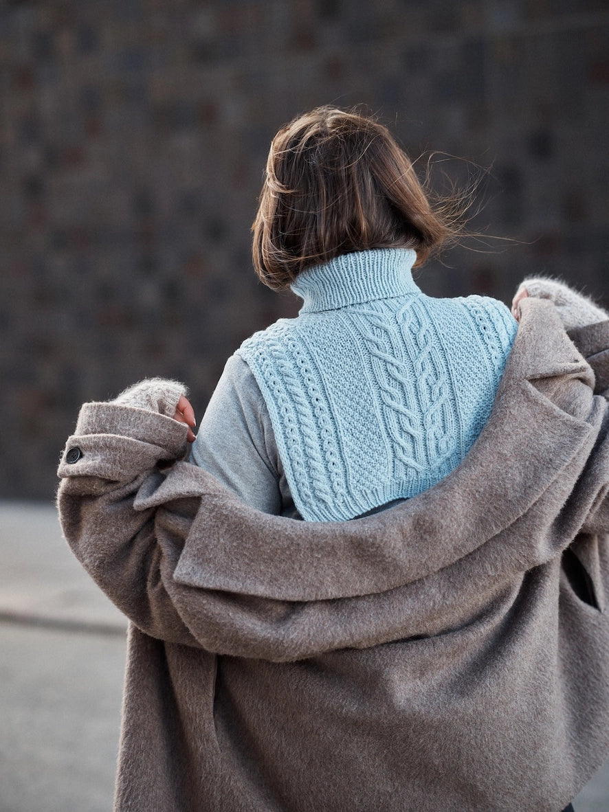Person wearing a blue knitted sweater and brown coat with a blurred background
