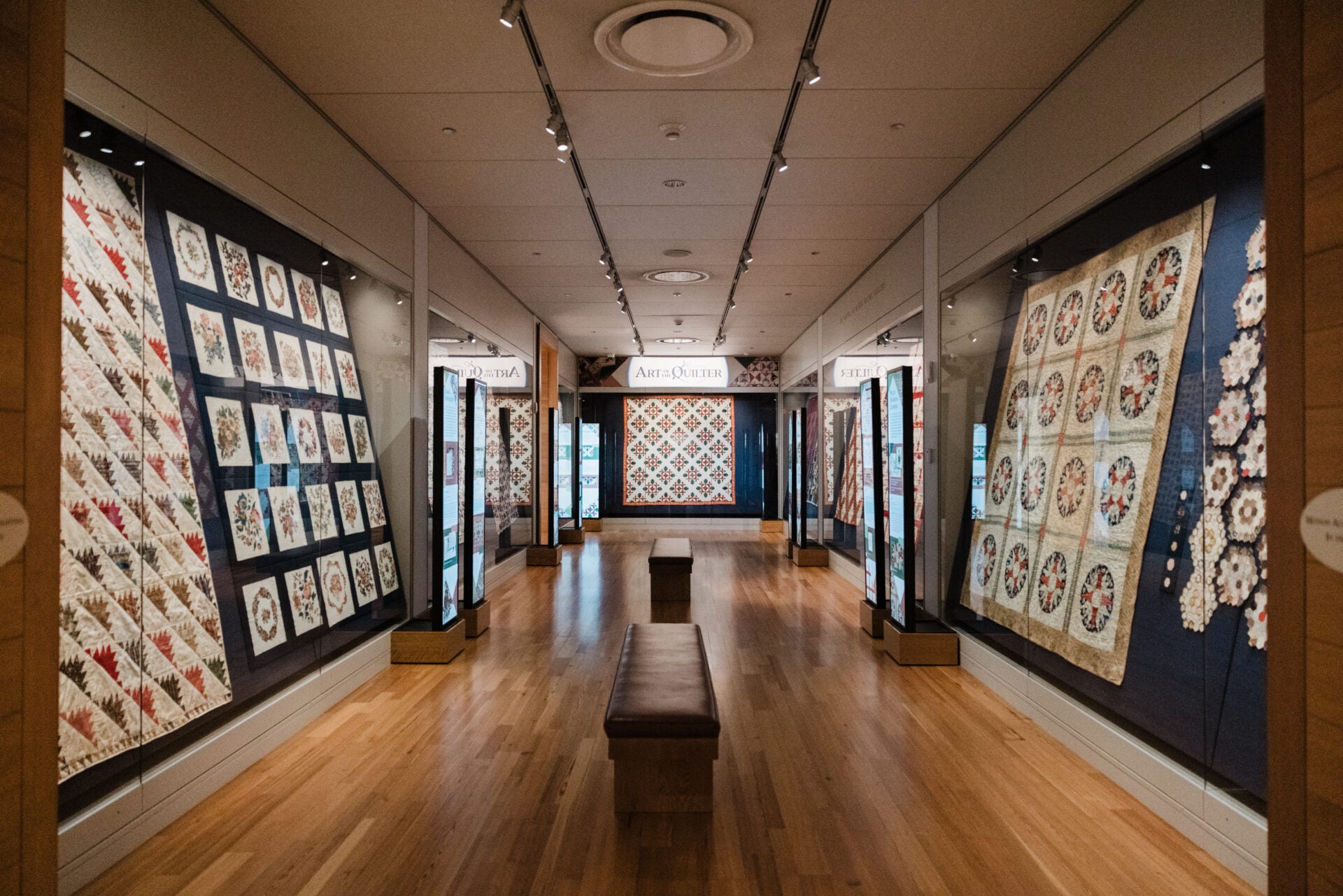 Museum exhibit with quilts displayed on walls.
