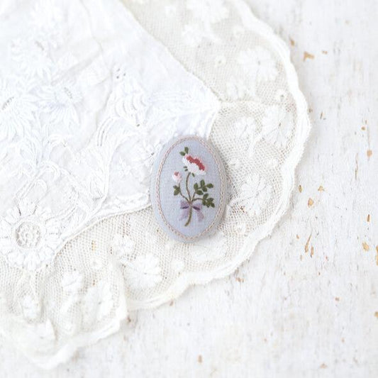 a blue embroidered broach on a piece of lace