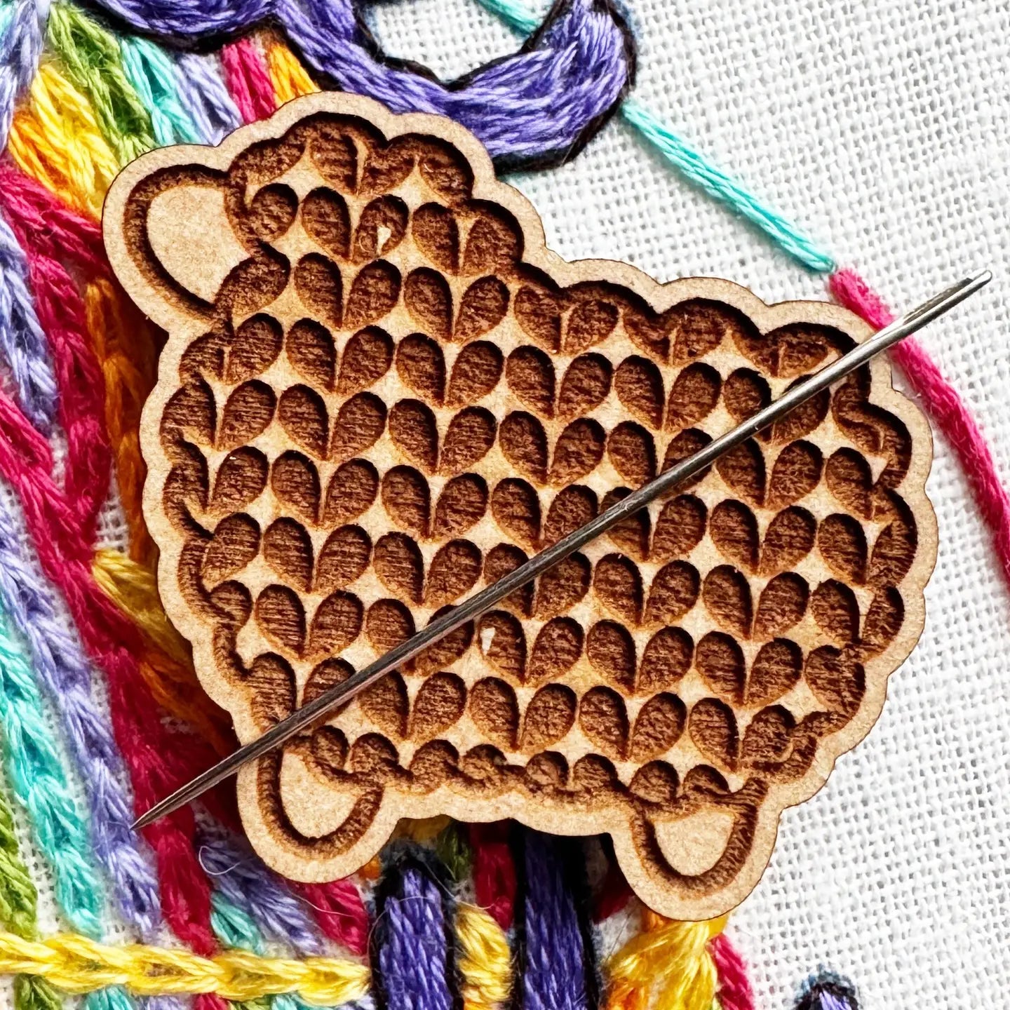 Wooden embroidery tool with colorful threads on a white fabric background