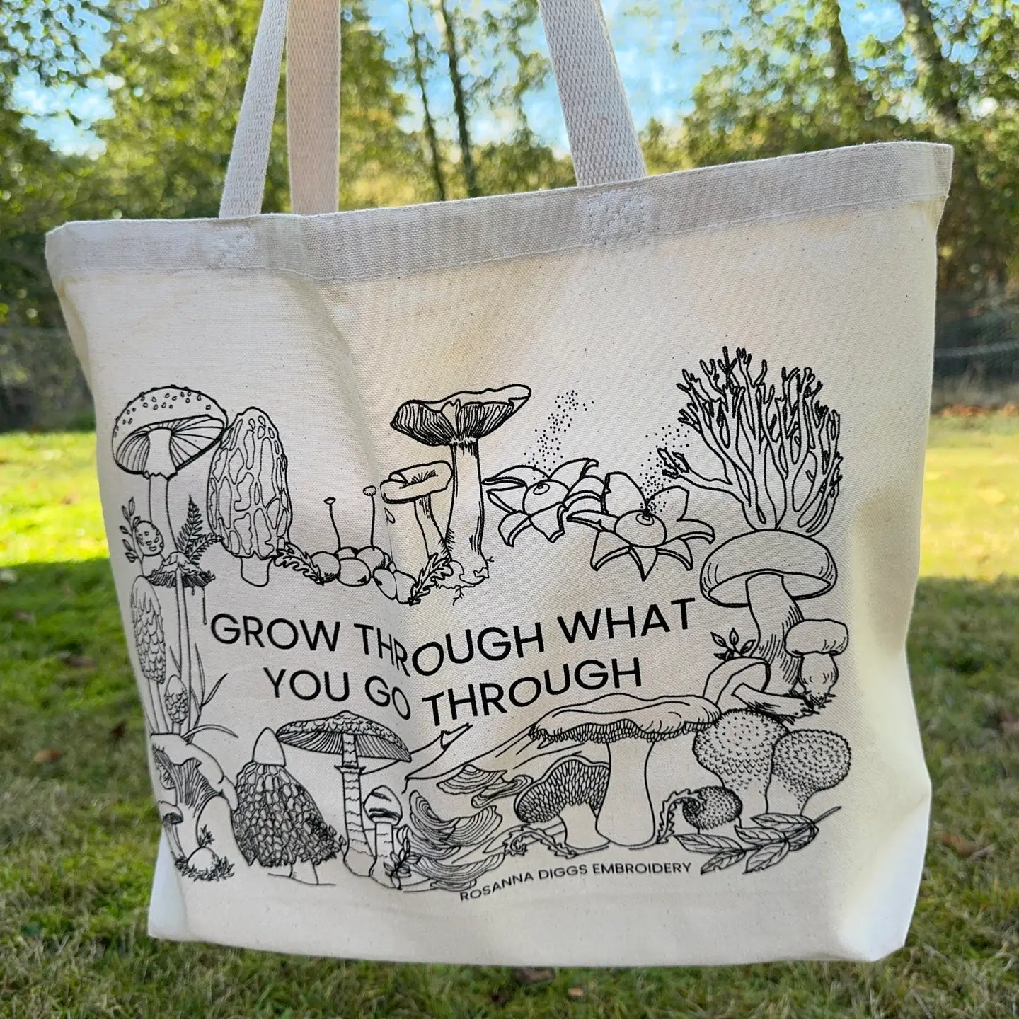 Tote bag with mushroom illustrations and text 'Grow through what you go through' on grass.