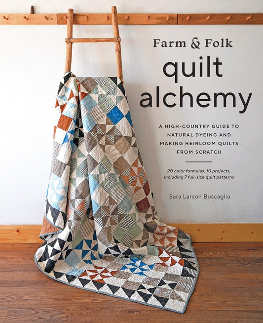 Quilt on a wooden floor with 'Farm & Folk quilt alchemy' book title above