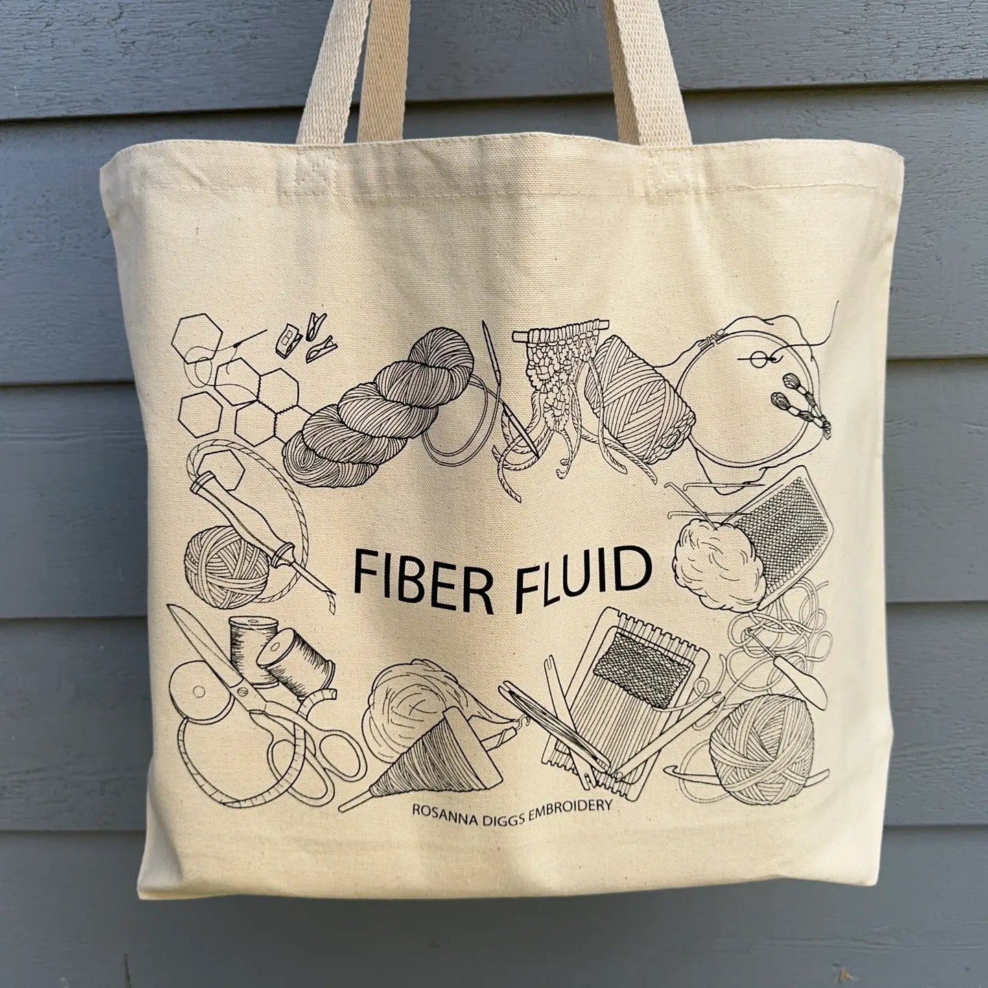 Tote bag with 'Fiber Fluid' design and illustrations on a gray background