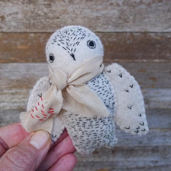 Small plush owl toy with a scarf held in a hand against a wooden background