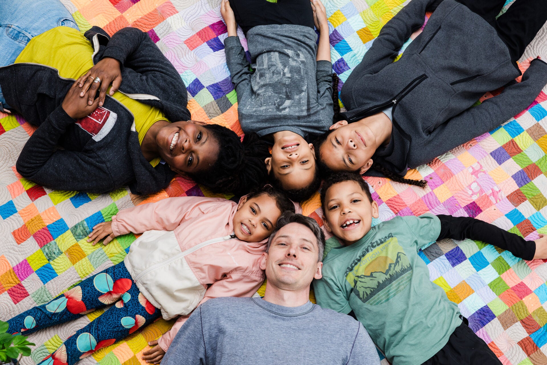 Children and a person lying on a colorful quilt