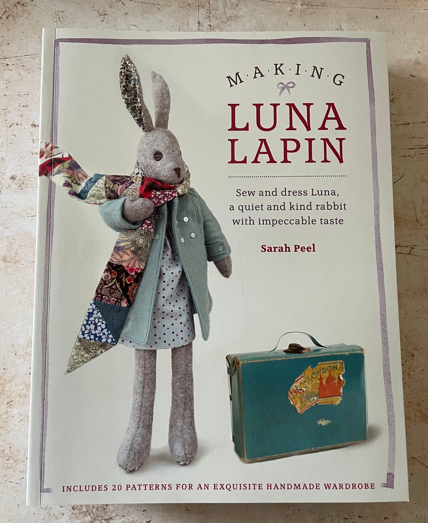 A felt sewn rabbit with a blue coat and a patchwork scarf and a blue suitcase