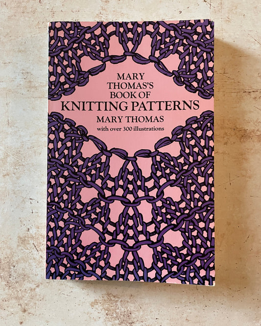 Book cover of 'Mary Thomas's Book of Knitting Patterns' with a pink and purple design on a textured beige background.