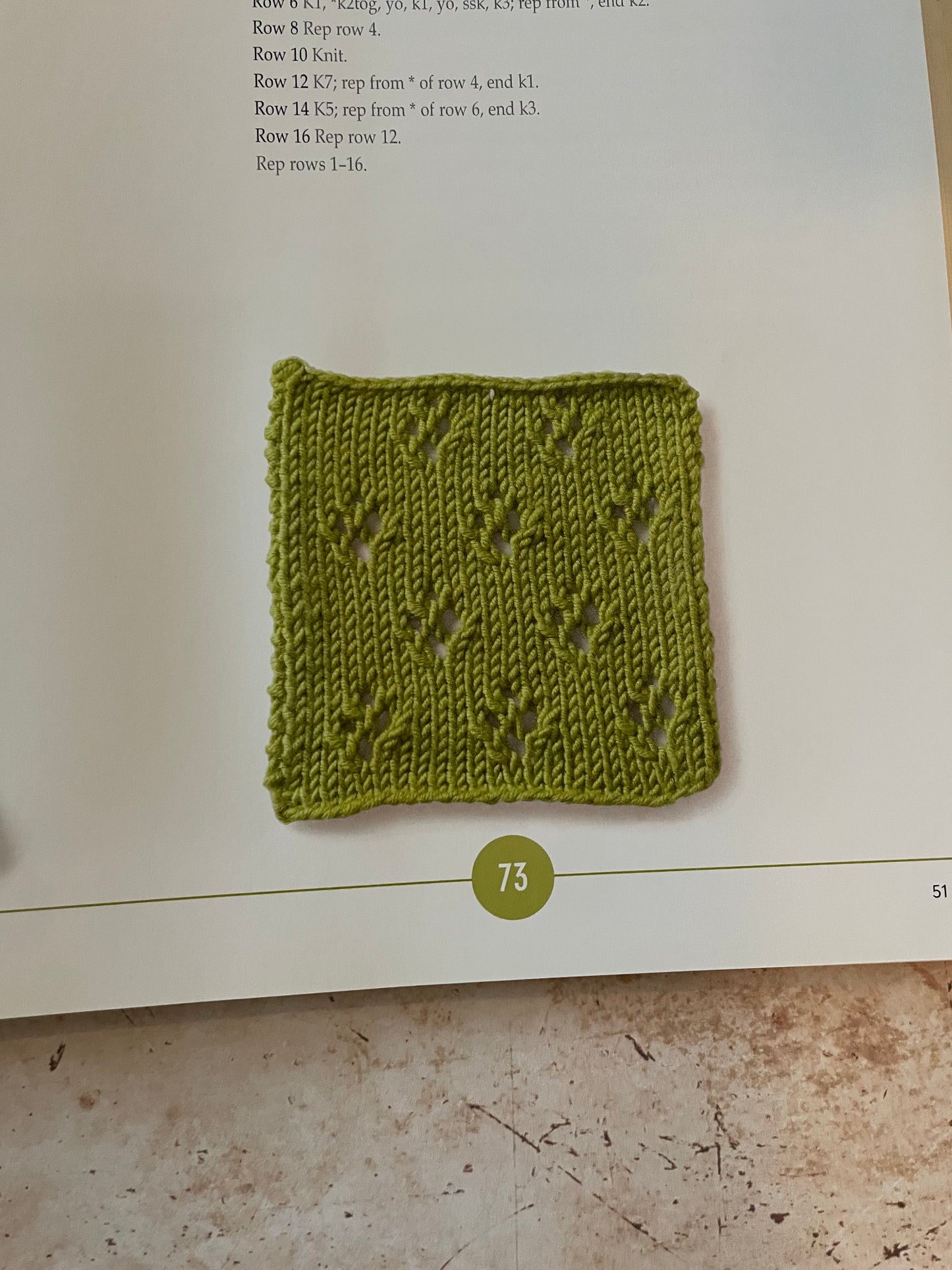Green knitted square on a book page with text and a number 73.