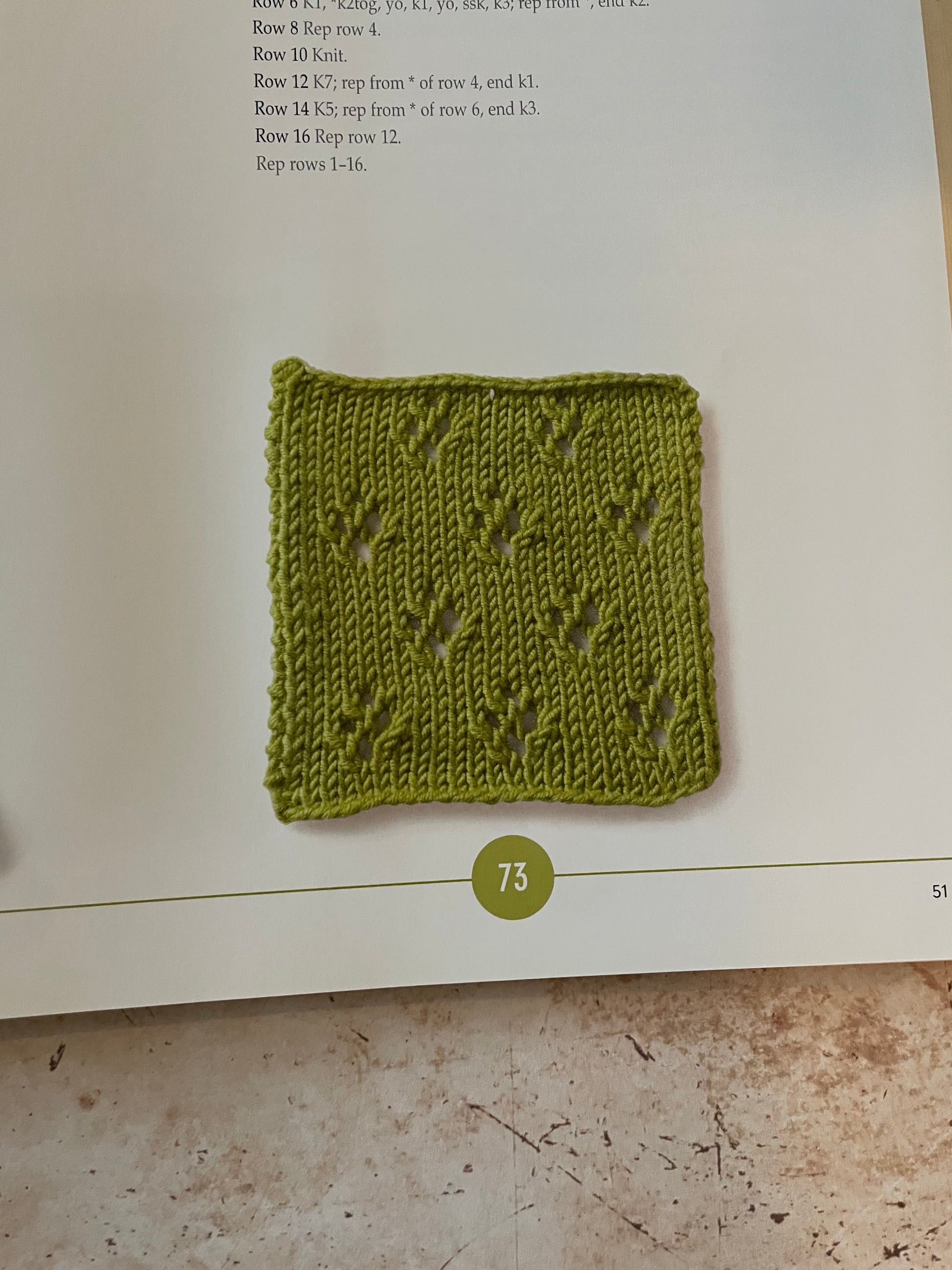 Green knitted square on a book page with text and a number 73.