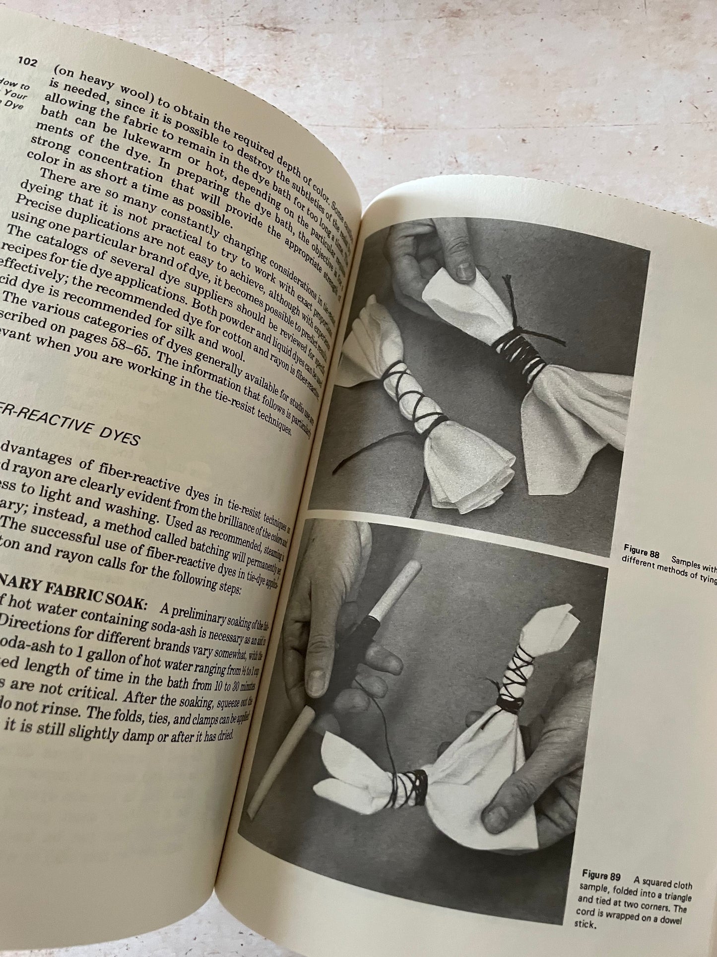 An open vintage book spread showing printed text on one page and a black-and-white photograph of a person holding a white lace-up cloth on the other page.