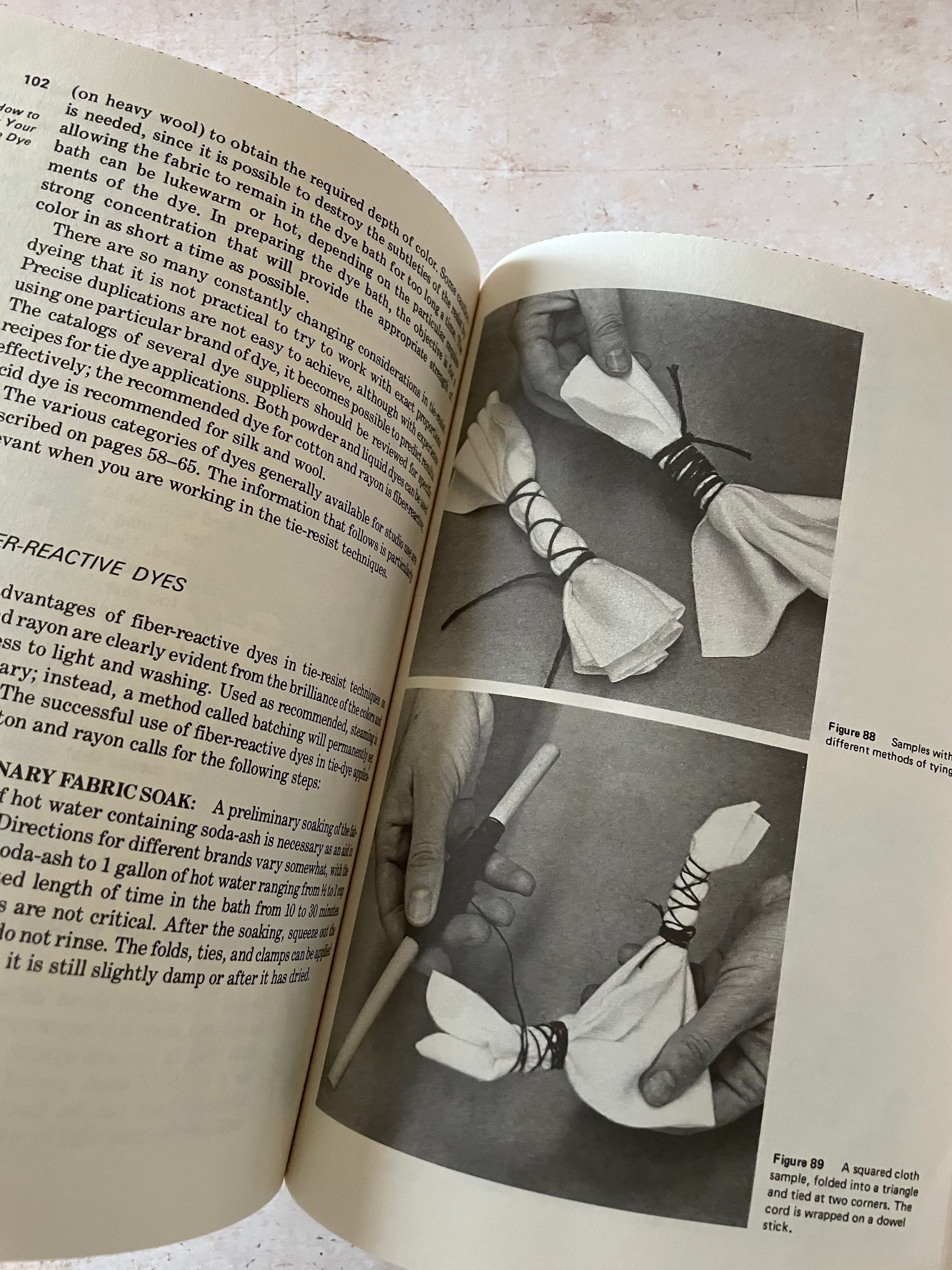 An open vintage book spread showing printed text on one page and a black-and-white photograph of a person holding a white lace-up cloth on the other page.