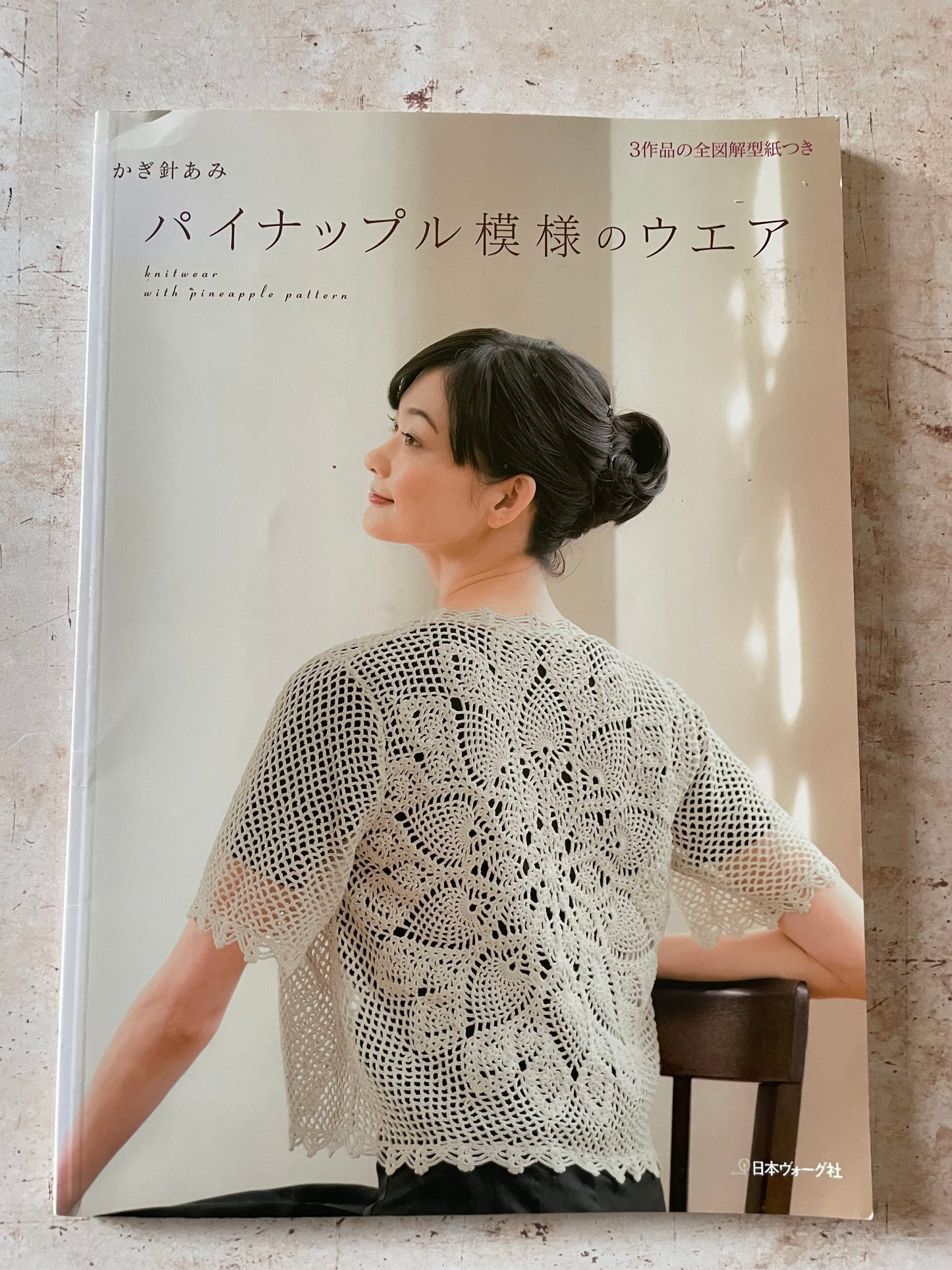 Japanese crochet pattern book featuring a photo of a woman wearing a white crochet short-sleeve top on the cover, set against a textured light gray background.