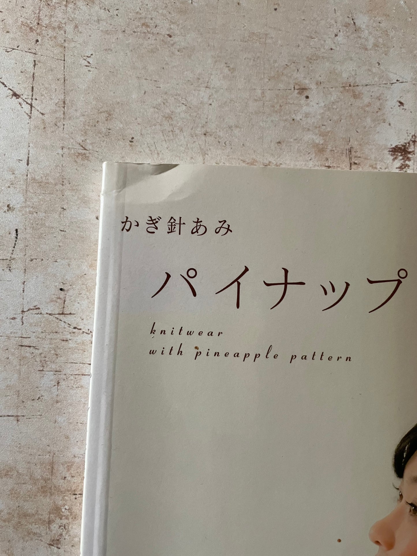 A close-up of a book  text 'knitwear with pineapple pattern' on a textured beige background. Shows corner indent
