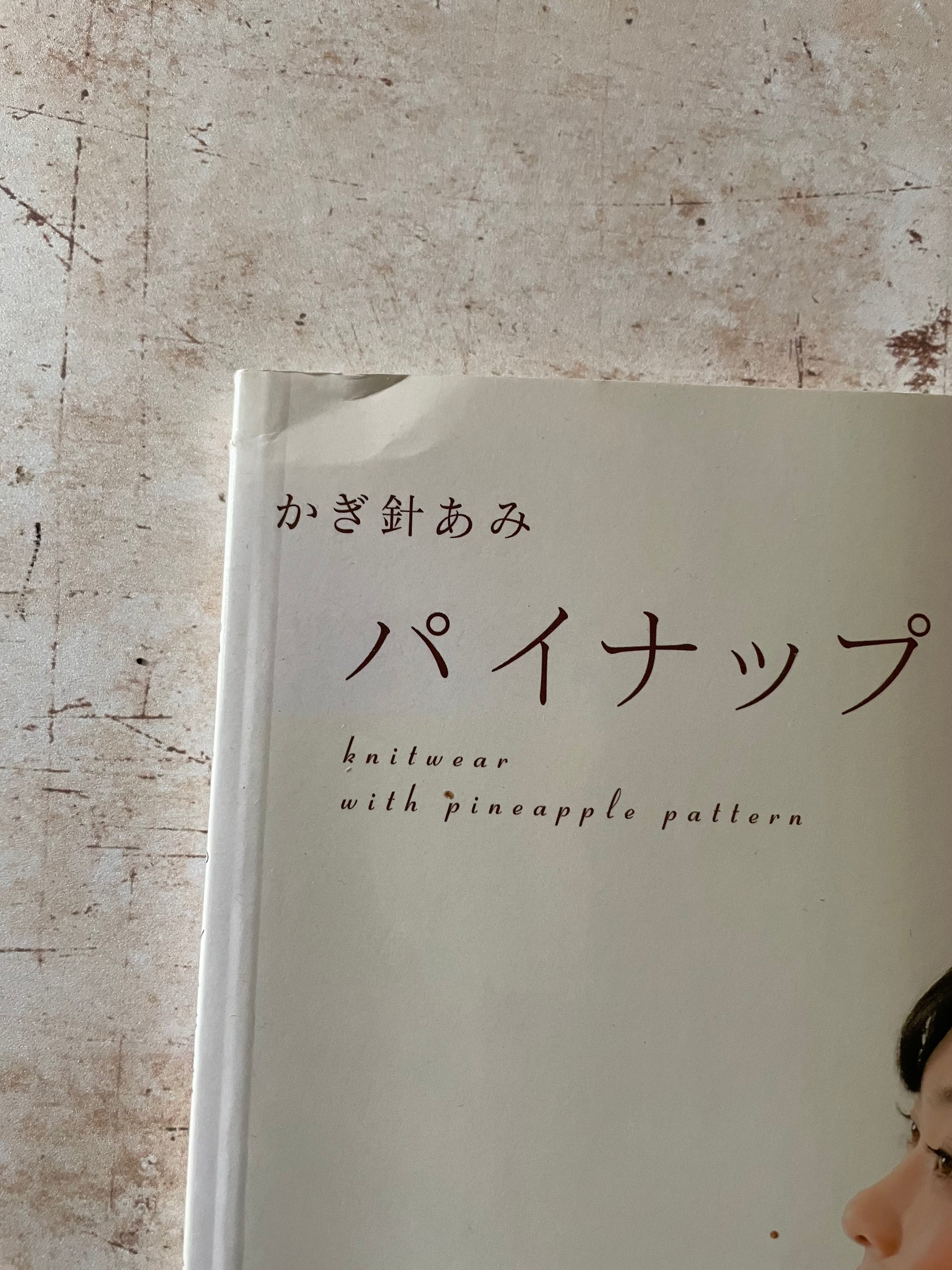 A close-up of a book  text 'knitwear with pineapple pattern' on a textured beige background. Shows corner indent