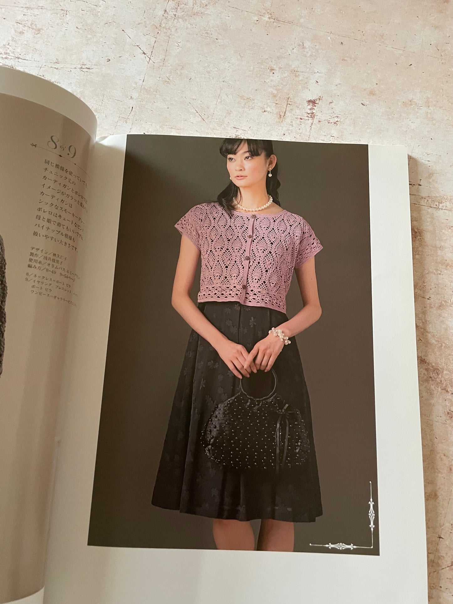 An open book or magazine spread showing a model wearing a lavender lace short-sleeve crop top and a black skirt.