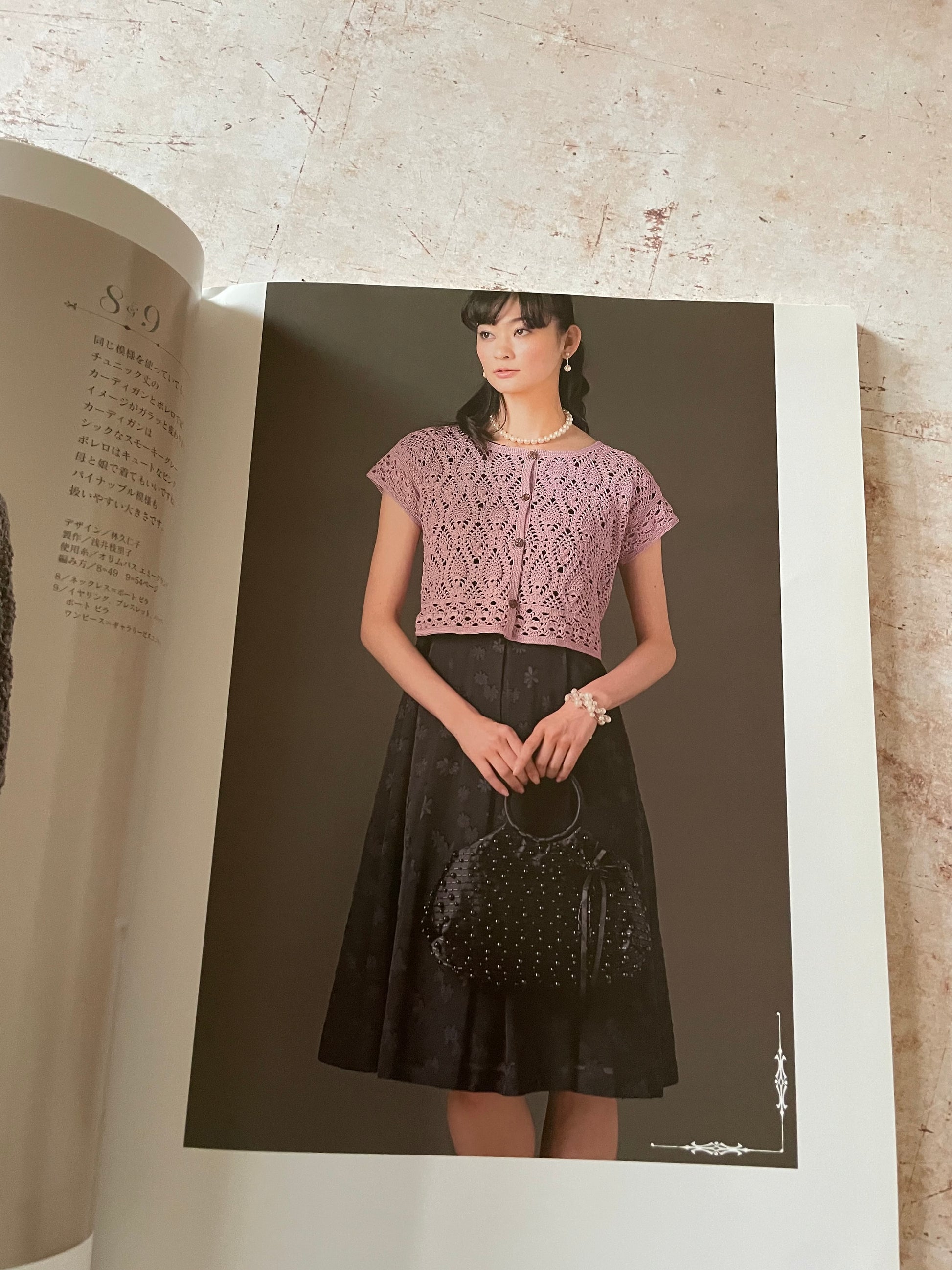 An open book or magazine spread showing a model wearing a lavender lace short-sleeve crop top and a black skirt.
