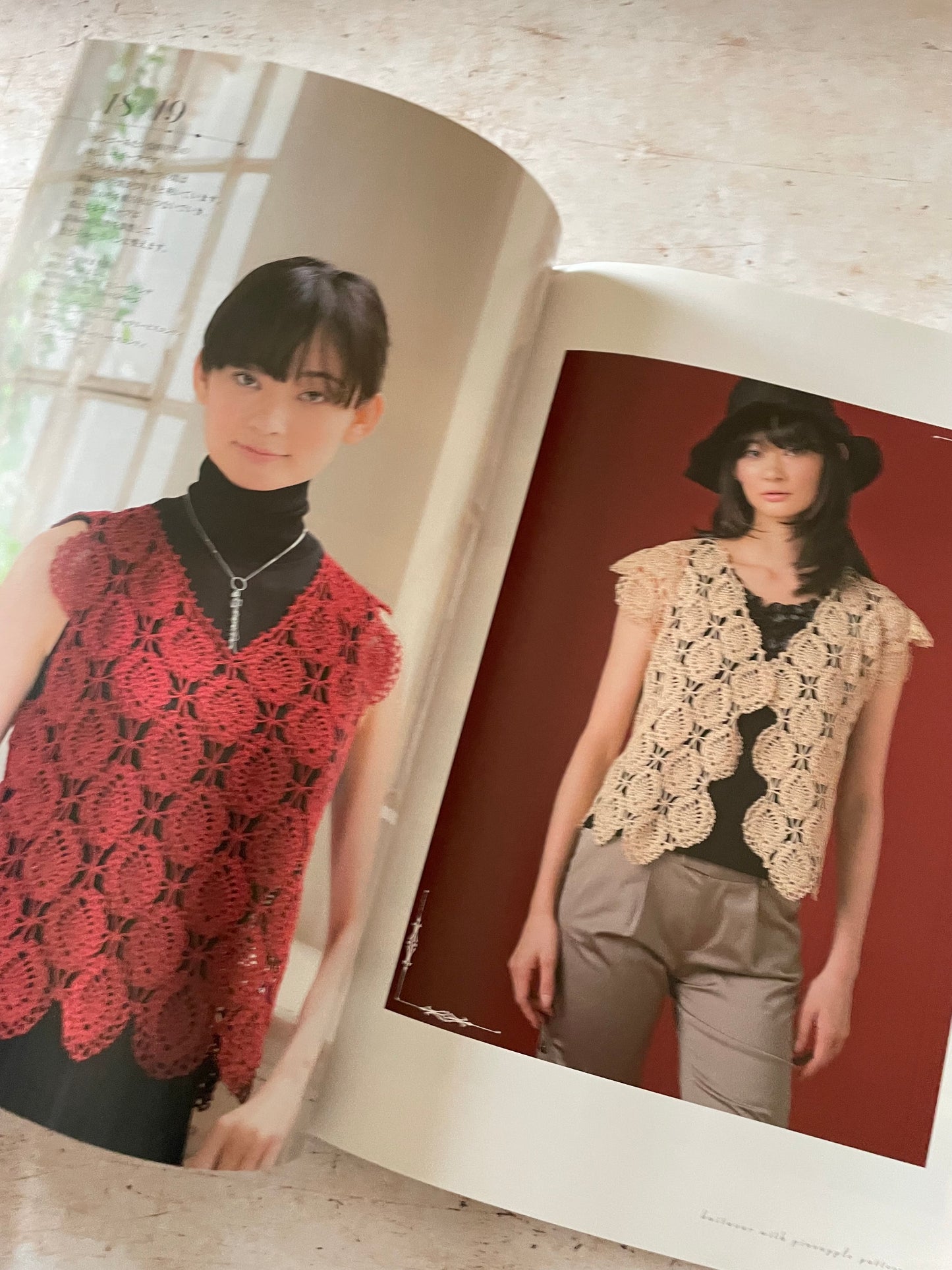 An open book showing two fashion photos of women wearing crocheted lace sleeveless tops. The left page shows a woman in a red lace top over a black turtleneck, and the right page shows a woman in a beige lace top with gray pants against a red studio background.