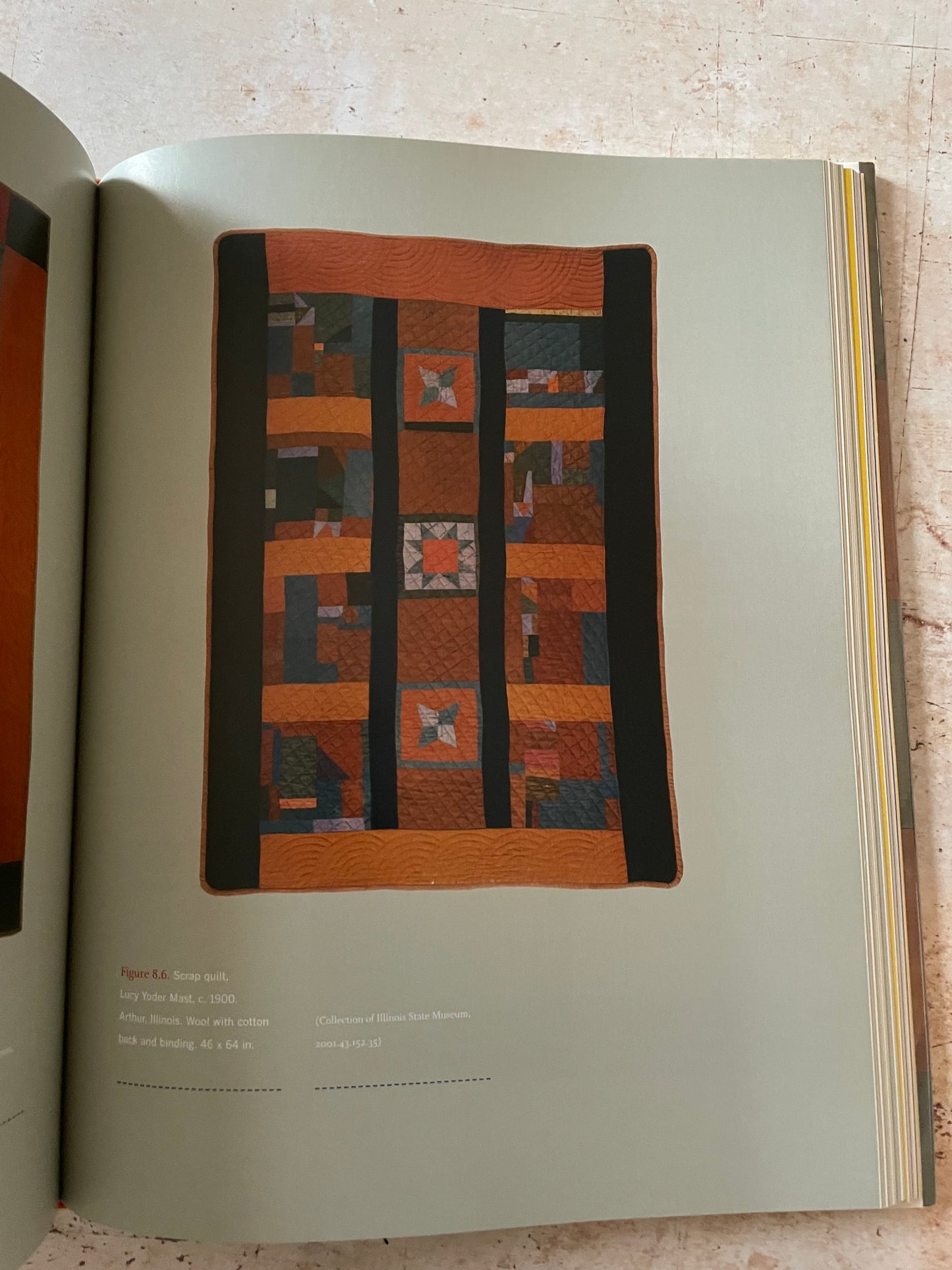 An open book  showing a quilt design page with a rectangular patchwork quilt illustration in the center. 