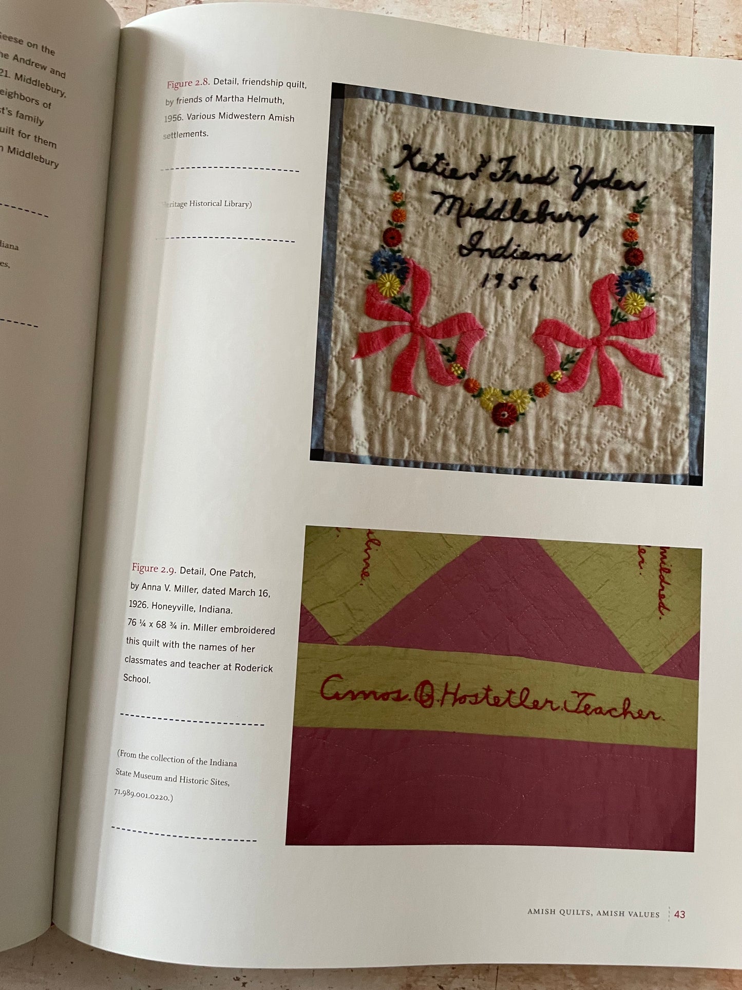 An open book showing printed pages with two quilt photos and handwritten notes. The top photo shows a quilt with embroidered bows and  text, and the bottom photo shows a quilt with geometric sections.
