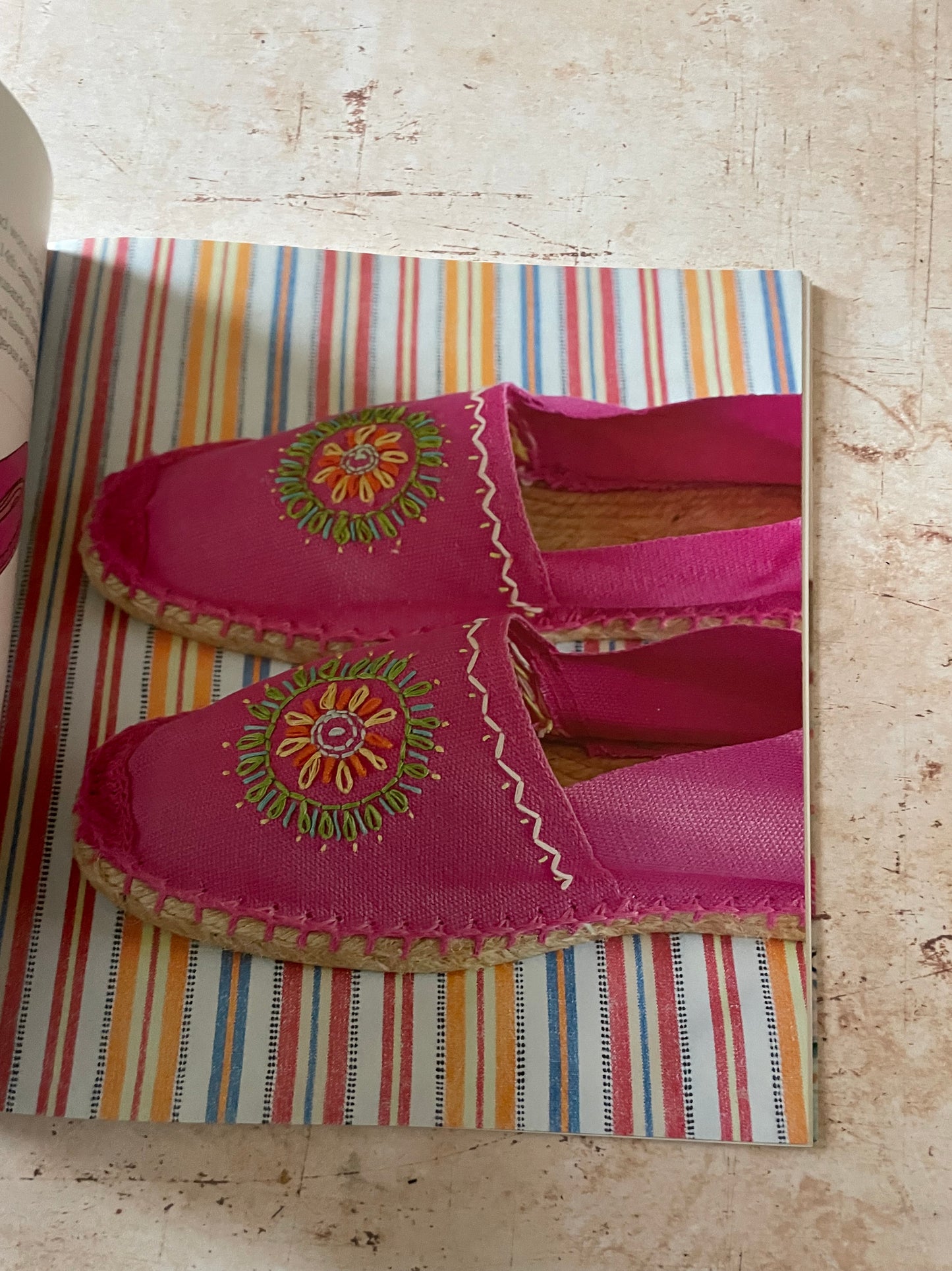 A pair of bright pink espadrille-style mule shoes with colorful embroidered floral details on the sides