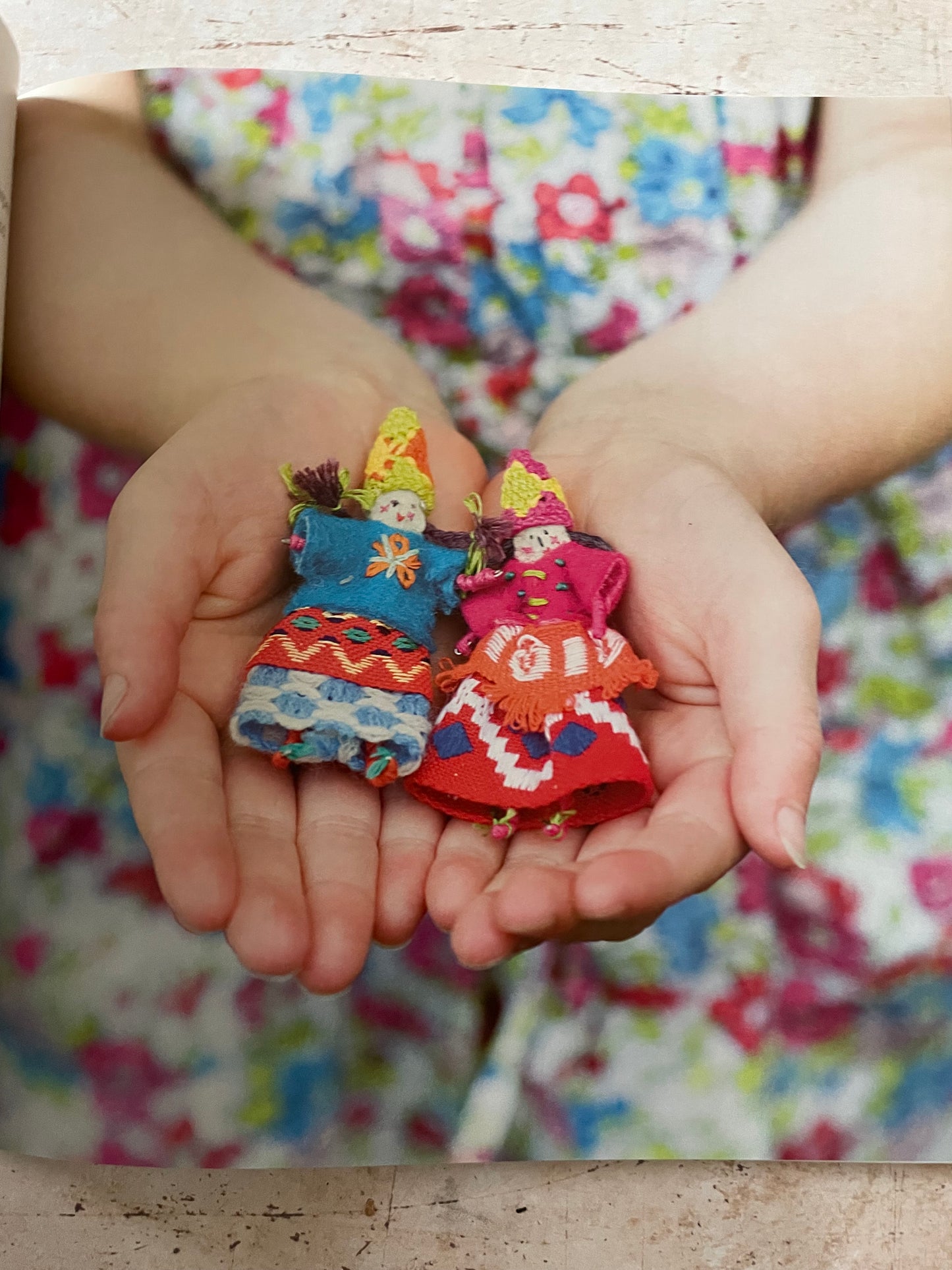 A close-up of a person's hands holding a small stack of colorful cloth dolls