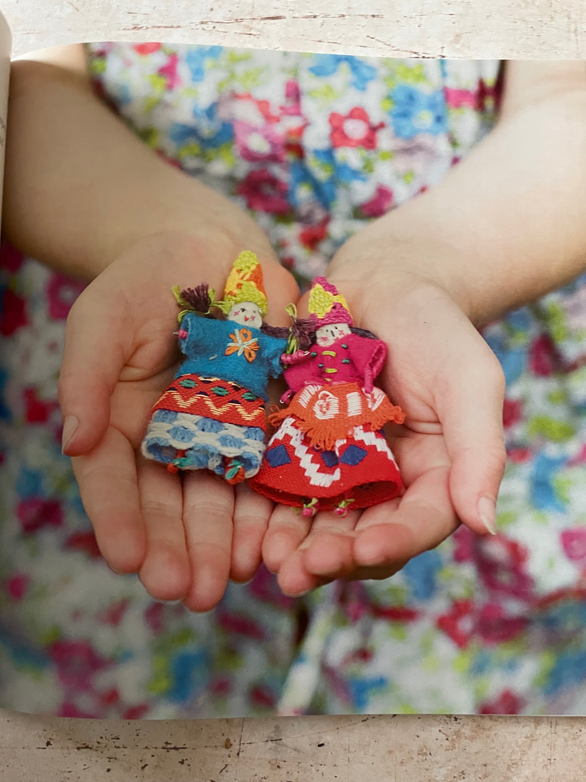 A close-up of a person's hands holding a small stack of colorful cloth dolls