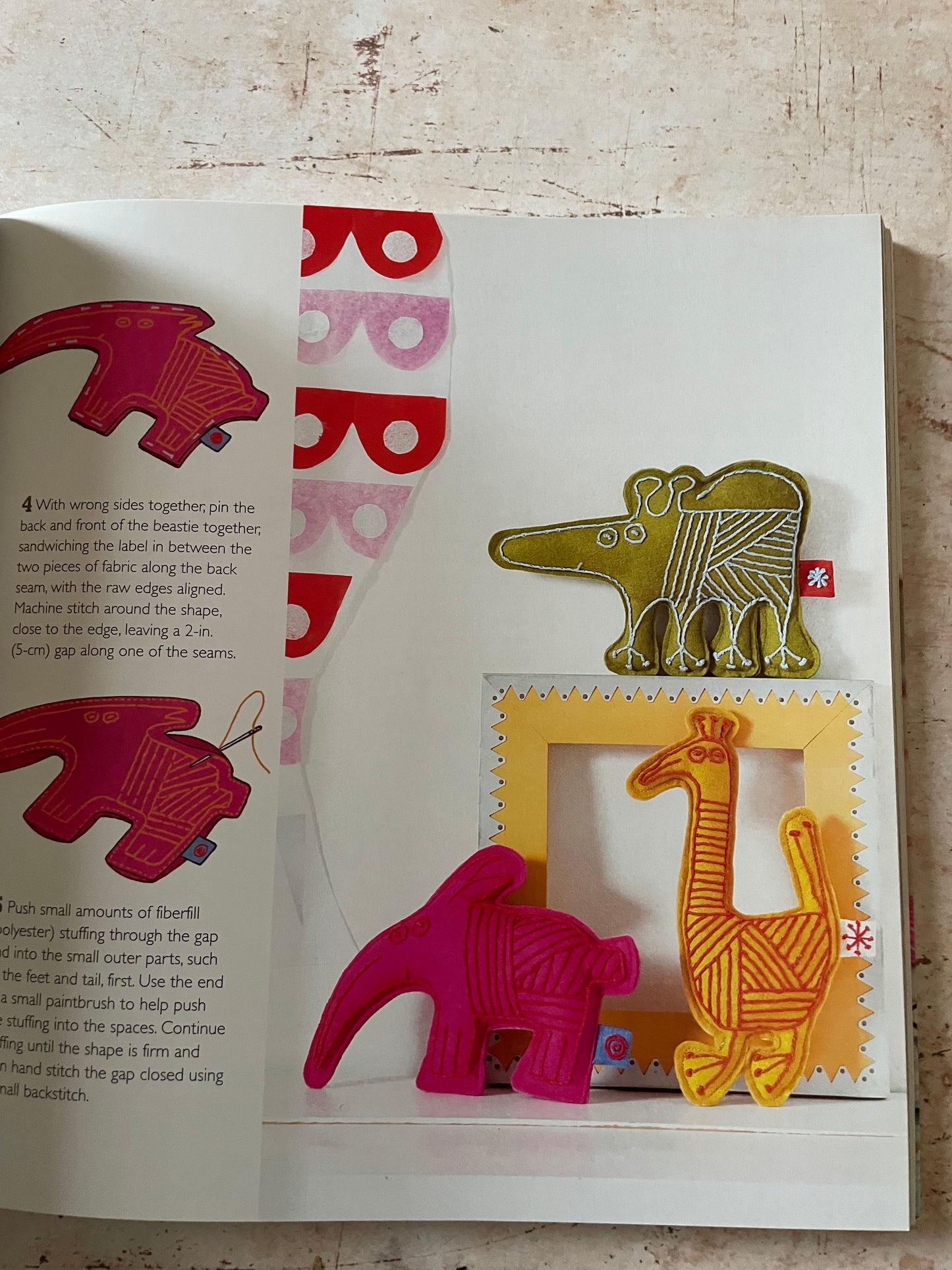 A set of colorful, camel-shaped fabric  displayed on a white sheet of paper over a rustic wooden surface. The set includes camels in olive green, yellow, and bright pink, along with a patterned banner and printed instructions below.