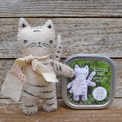 Stuffed cat toy with a tin containing another small cat figure on a wooden surface
