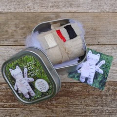 Small plush toy in a tin with packaging on a wooden surface