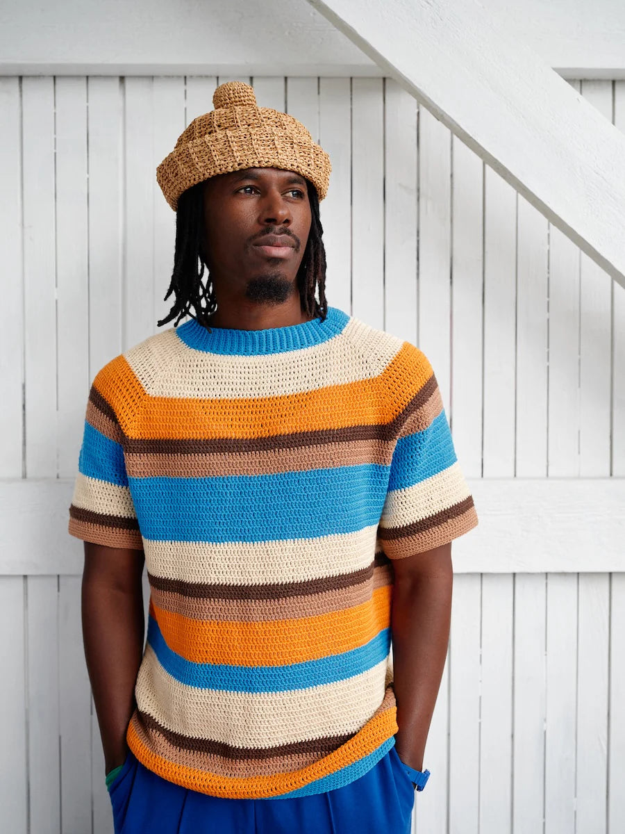 Man wearing a colorful striped sweater and beanie against a white wooden background