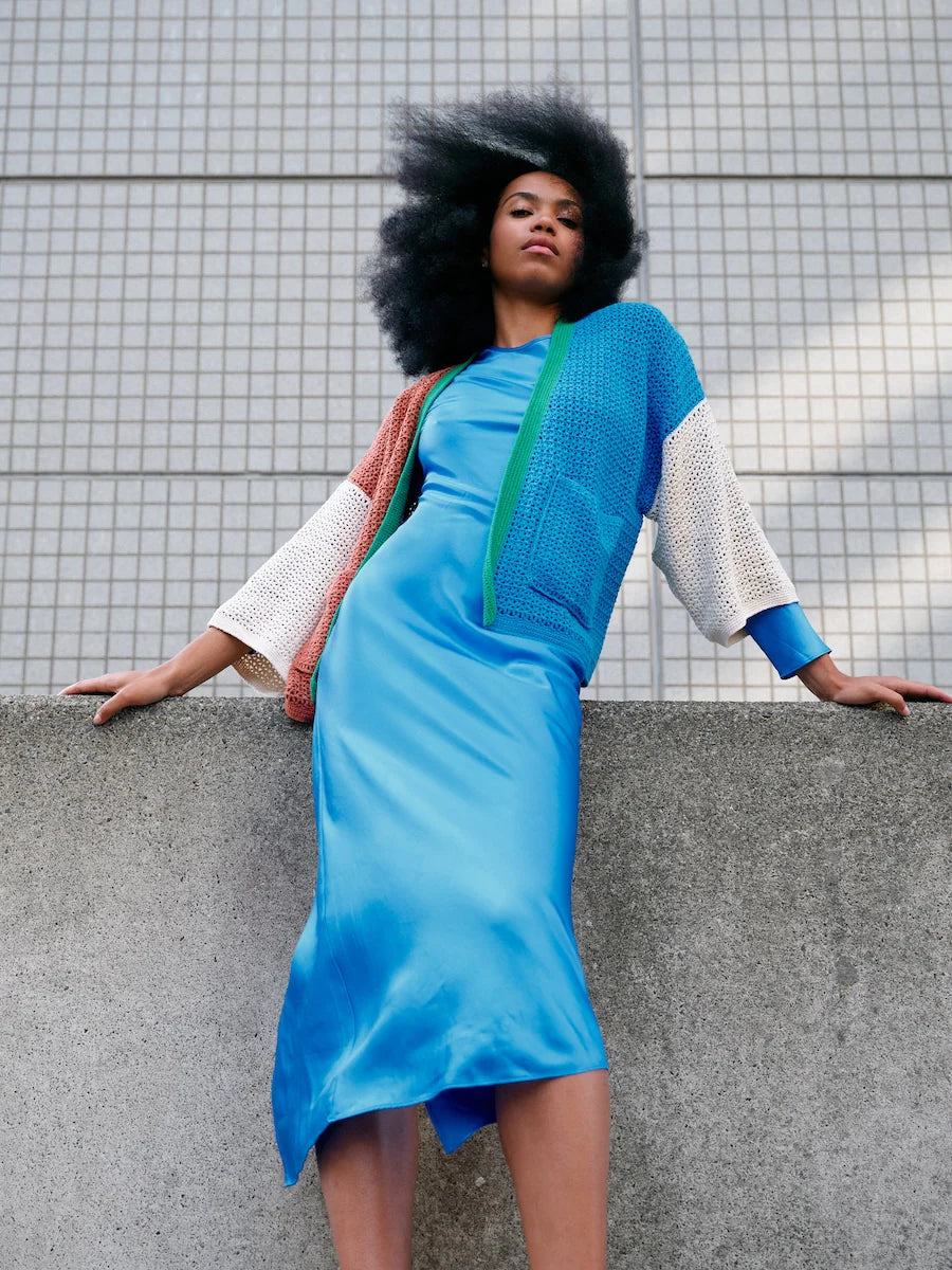 Woman wearing a blue dress and green cardigan against a tiled wall.