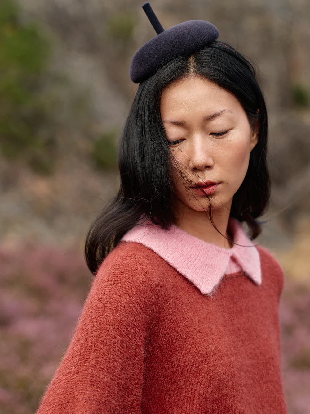 Woman wearing a red sweater with a pink collar and a dark beret in a natural setting.