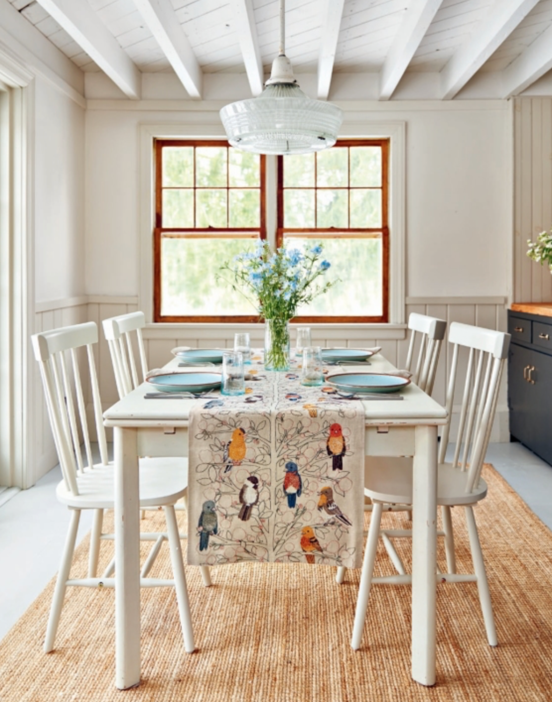 A white table and chairs with a bird embroidered table runner