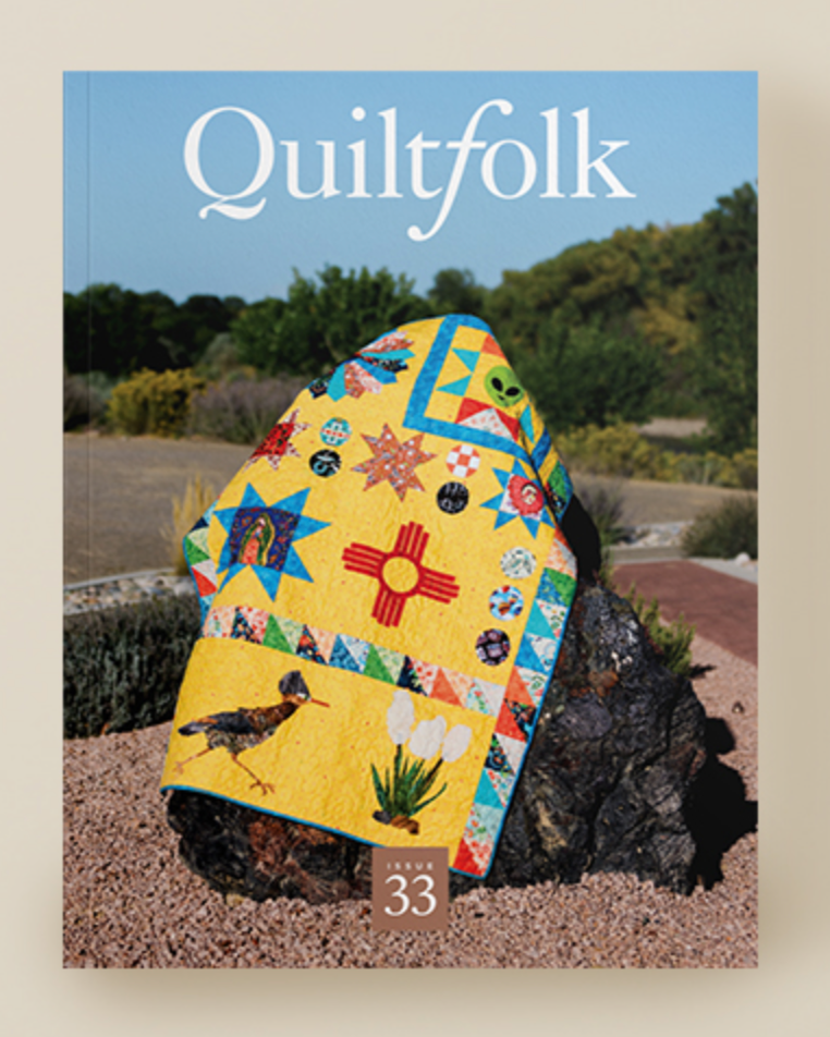 A yellow quilt with colorful imagery on a rock