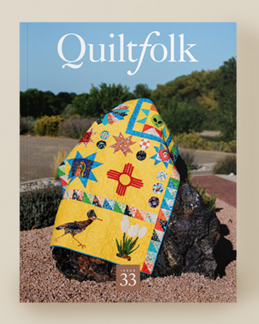 A yellow quilt with colorful imagery on a rock