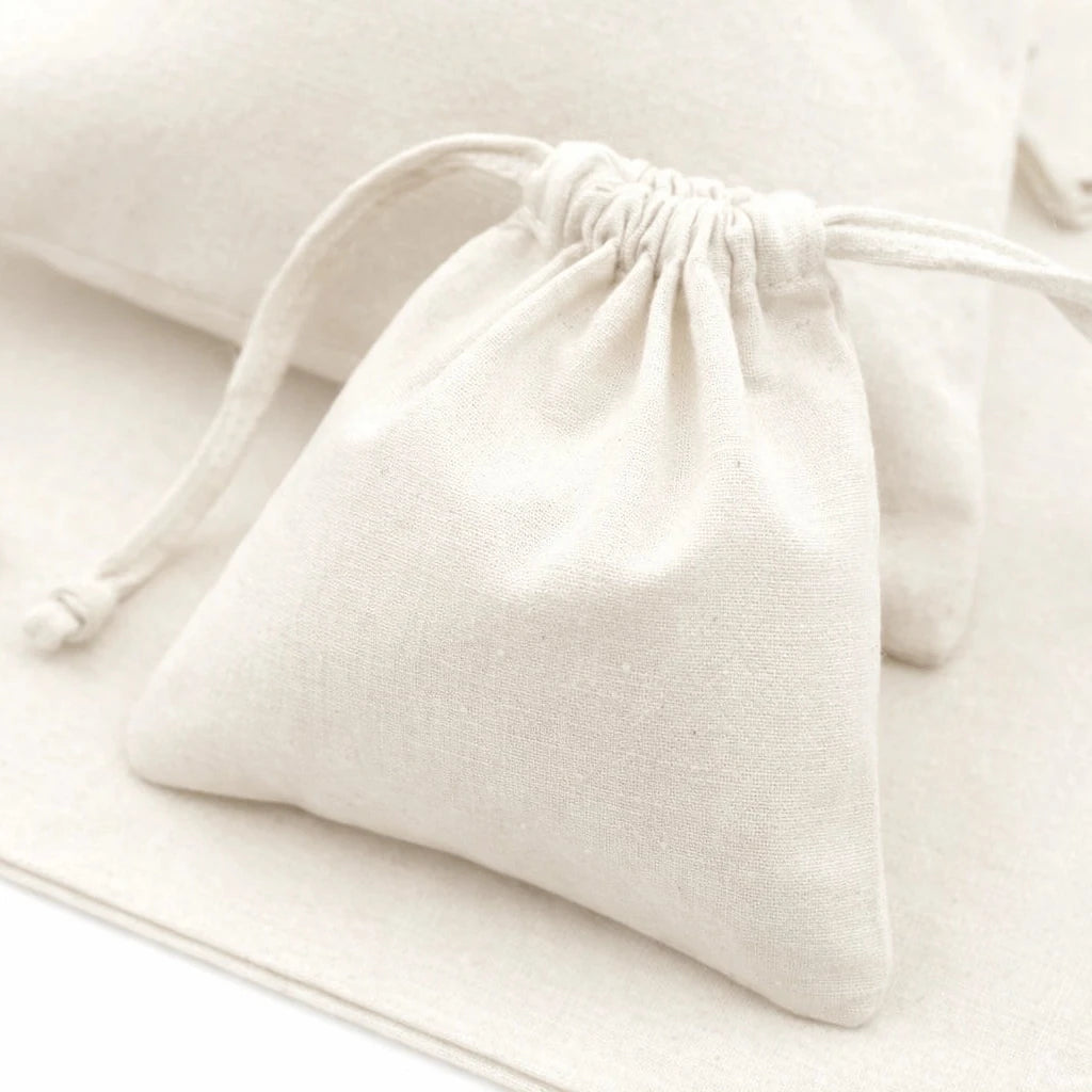 White drawstring bag on a light beige surface with a small silver ring beside it.