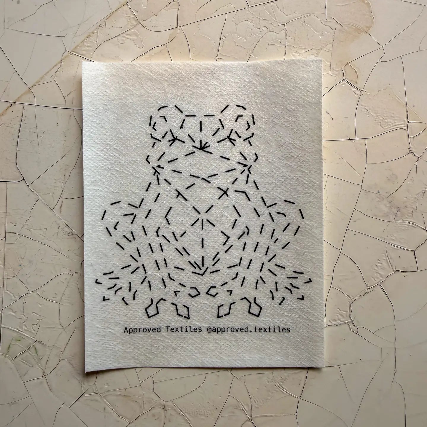 Textile sample with black geometric frog pattern on a textured beige surface