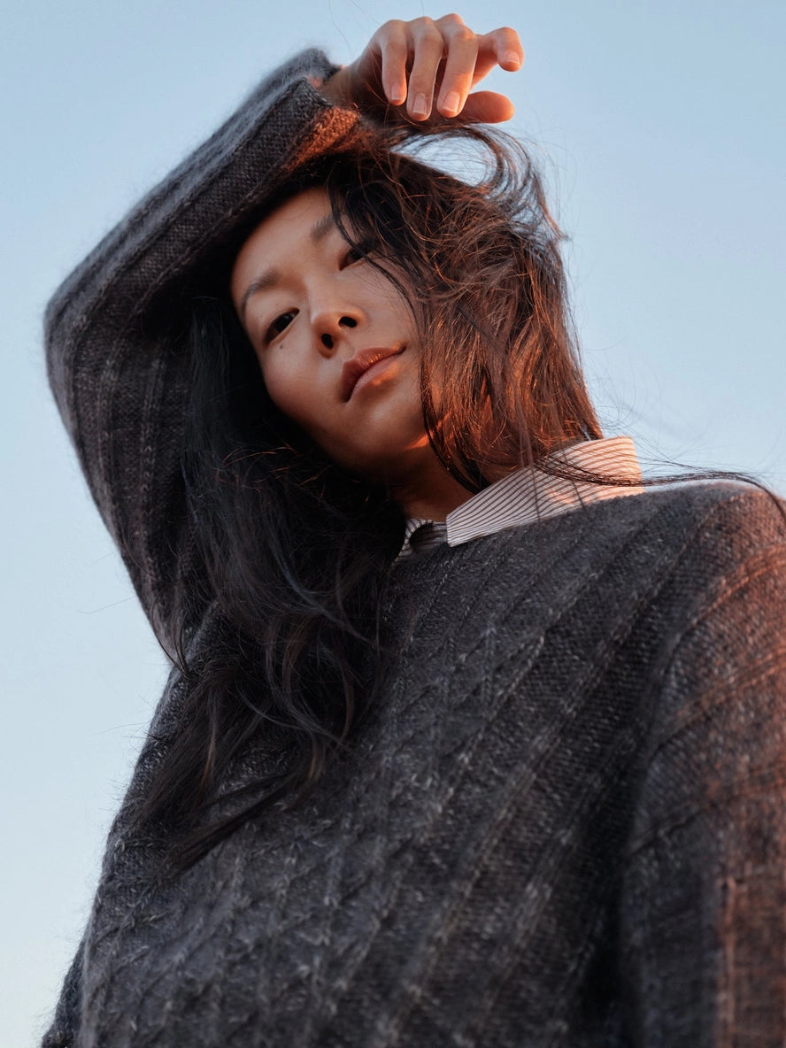Woman wearing a dark gray cabled sweater against a light blue sky.