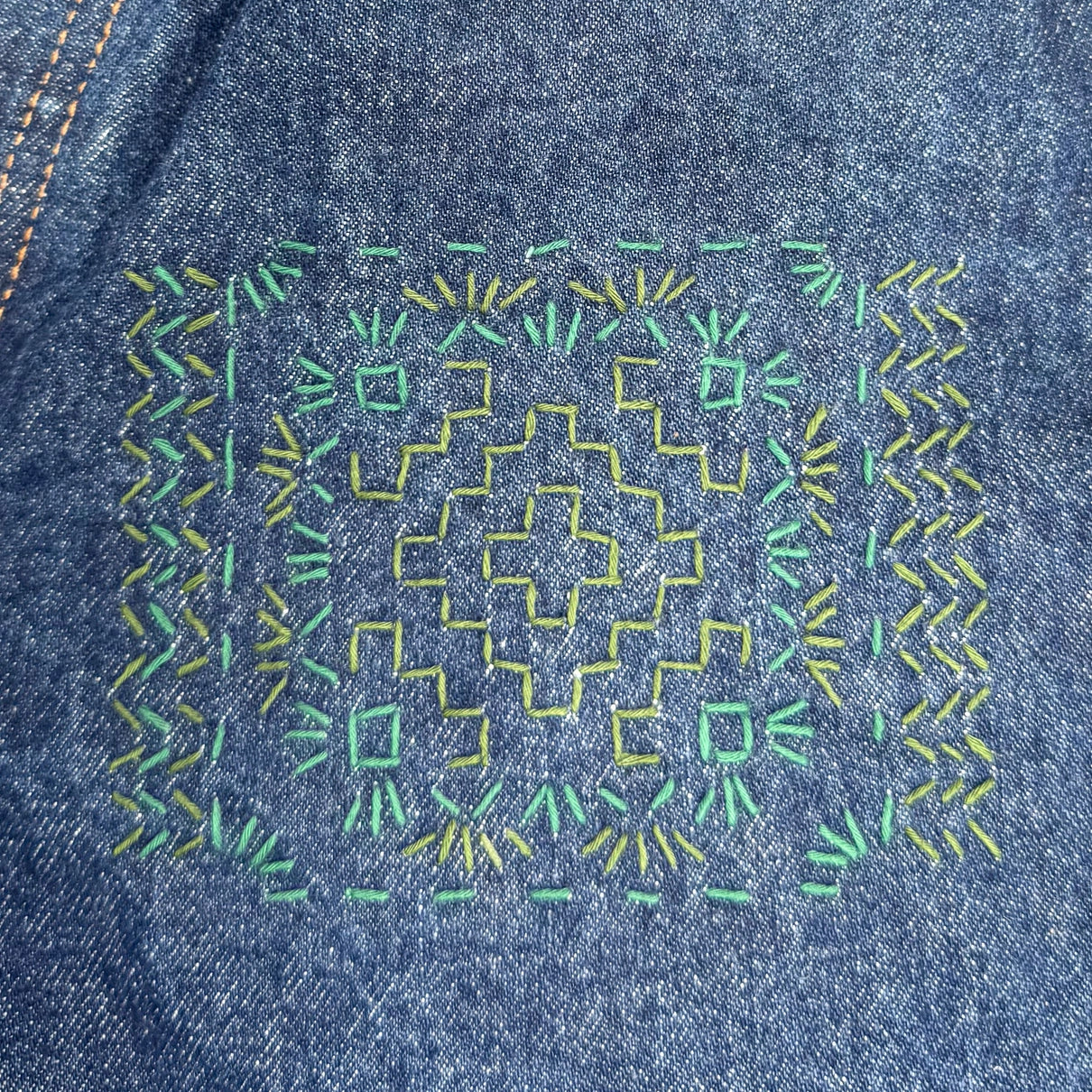 Close-up of denim fabric with green and yellow embroidery pattern