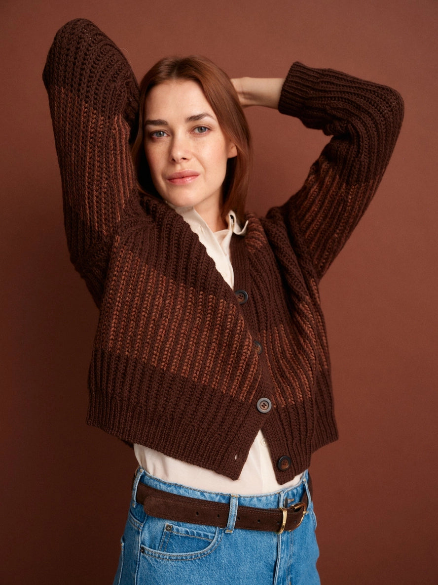 Woman wearing a brown knitted cardigan over a white shirt with a brown background