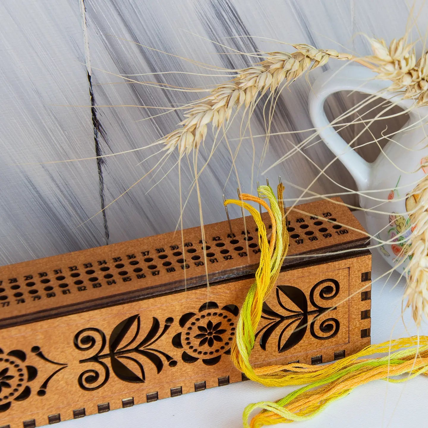 Wooden box with floral patterns and a spool of thread, with wheat ears in the background.