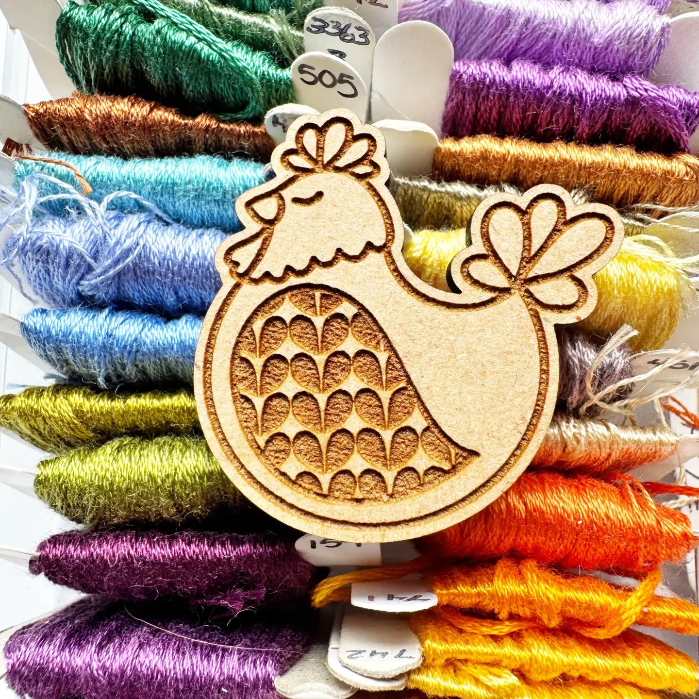 Wooden chicken-shaped embroidery tool surrounded by colorful thread spools