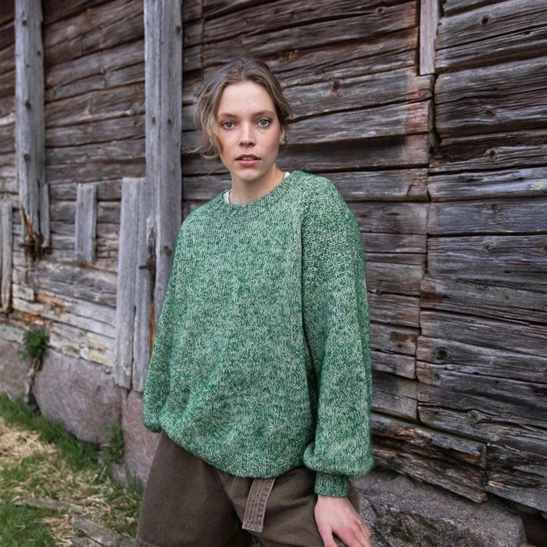 Person wearing a green sweater and brown shorts standing in front of a wooden building.